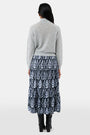 A woman with long dark hair is wearing the Roller Rabbit Heather Sequins Felice Sweater and a navy blue skirt with a white floral pattern, standing against a plain white background.