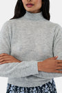 A woman with long dark hair is wearing the Roller Rabbit Heather Sequins Felice Sweater and a navy blue skirt with a white floral pattern, standing against a plain white background.