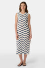 A woman wears the Roller Rabbit Zig Zag Irene Cover Up, a sleeveless, ankle-length crochet maxi dress with a blue and white zig zag pattern. She pairs it with black sandals and chunky striped bracelets, her straight brown hair worn loose.