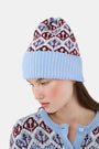 A young woman with fair skin and light makeup gazes at the camera, one hand on her hat, wearing a light blue Roller Rabbit Jemina Fairisle Beanie with a red and white pattern that matches her sweater.