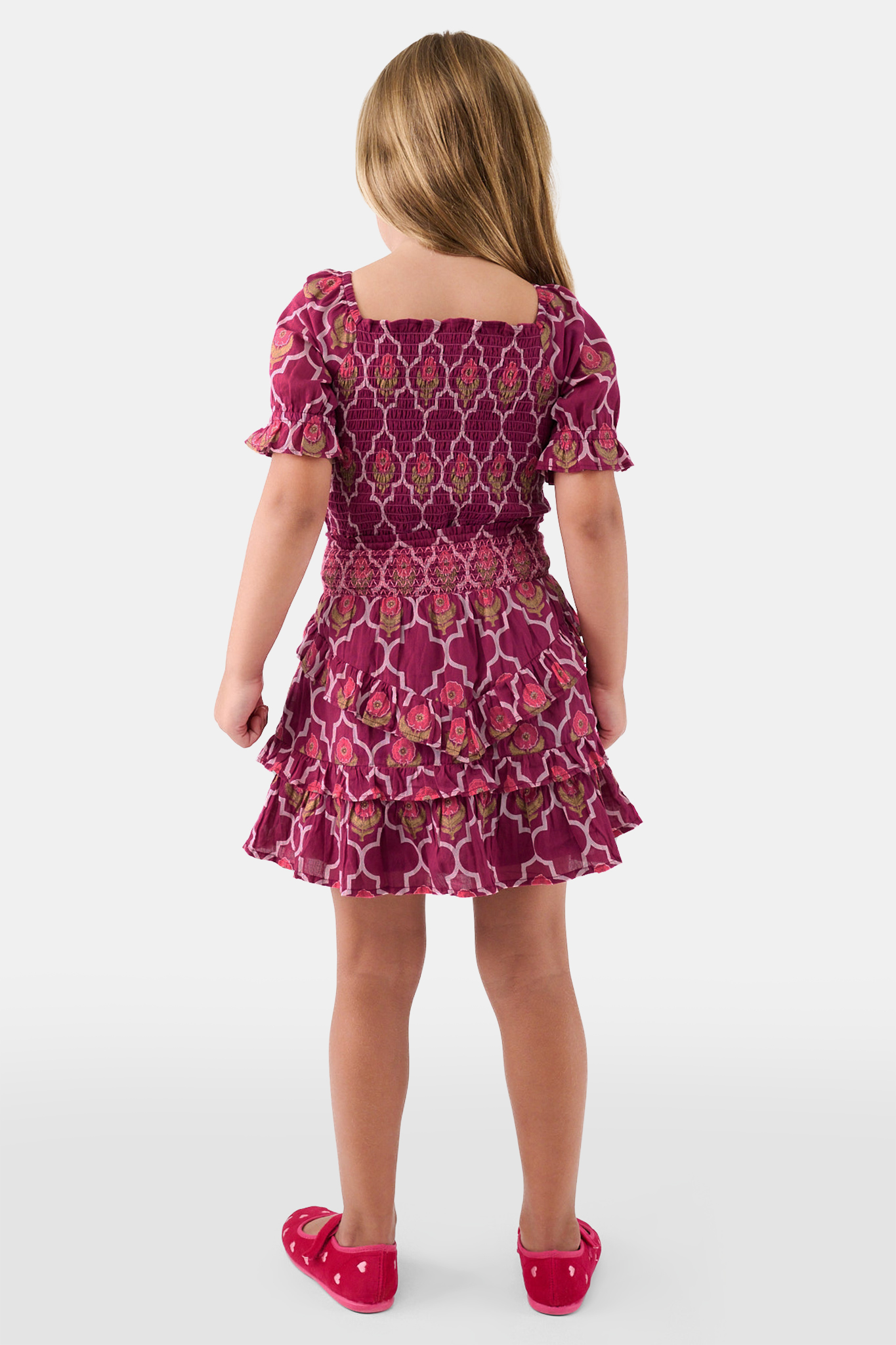 A young child wears the Roller Rabbit Kids Marquis Floral Bibi Skirt paired with maroon heart-accented shoes, standing against a plain white background.