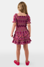 A young child wears the Roller Rabbit Kids Marquis Floral Bibi Skirt paired with maroon heart-accented shoes, standing against a plain white background.