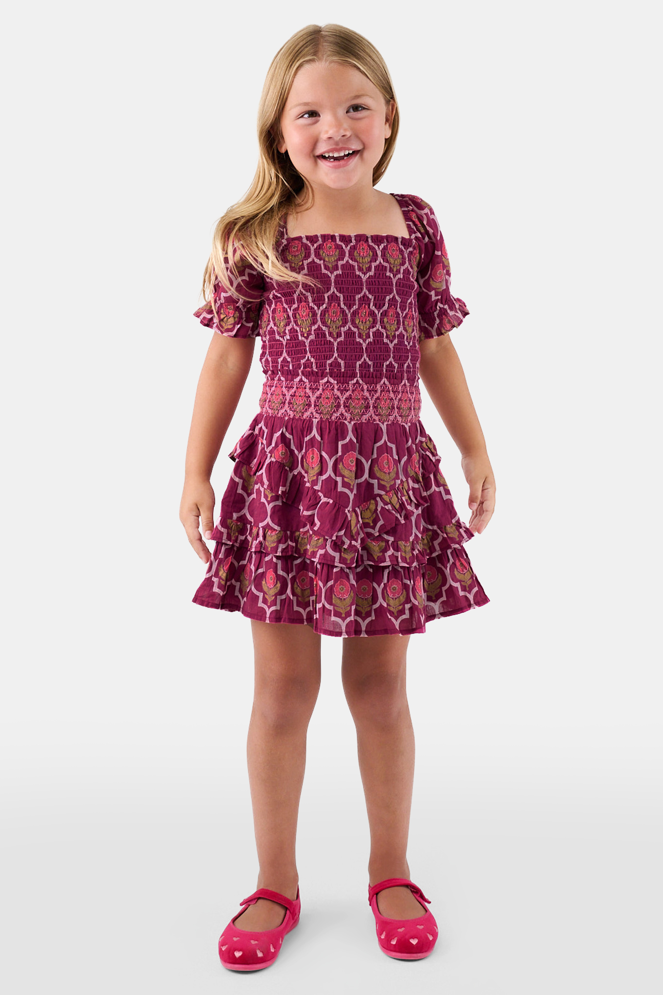 A young child wears the Roller Rabbit Kids Marquis Floral Bibi Skirt paired with maroon heart-accented shoes, standing against a plain white background.