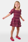 A young child wears the Roller Rabbit Kids Marquis Floral Bibi Skirt paired with maroon heart-accented shoes, standing against a plain white background.