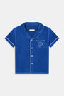 A young child wearing the Roller Rabbit Kids Monkey Embroidery Leo Polo—a navy top with white trim and an embroidered monkey on the chest pocket—smiles with arms raised overhead.