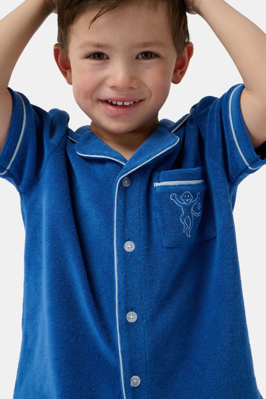 A young child wearing the Roller Rabbit Kids Monkey Embroidery Leo Polo—a navy top with white trim and an embroidered monkey on the chest pocket—smiles with arms raised overhead.