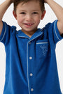 A young child wearing the Roller Rabbit Kids Monkey Embroidery Leo Polo—a navy top with white trim and an embroidered monkey on the chest pocket—smiles with arms raised overhead.