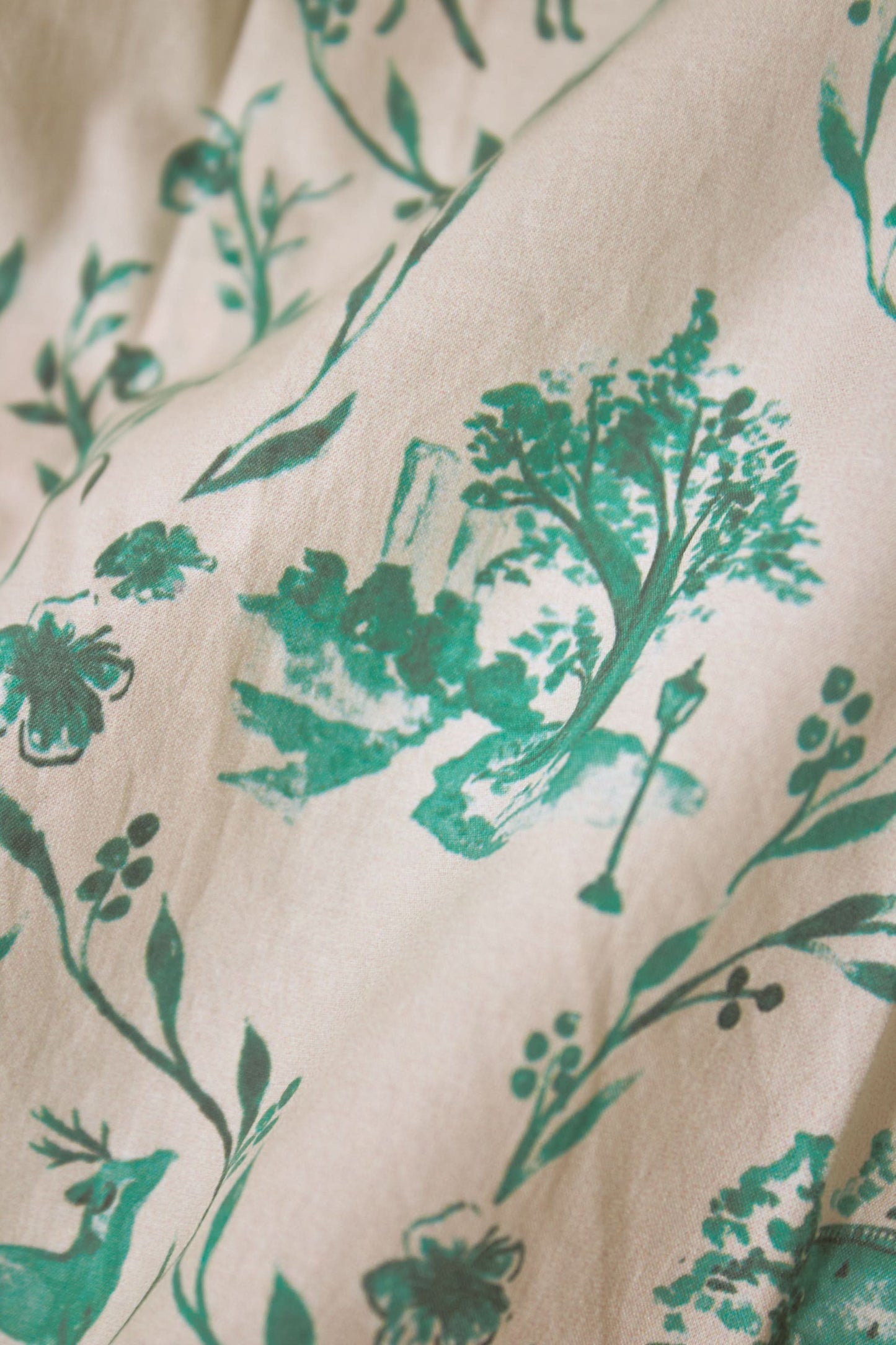 A person wears the Roller Rabbit Woodland Toile Quilted Azure Mini Skirt, featuring green floral patterns, green trim, a side slit, and paired with a matching white jacket—an ideal fall fashion ensemble.