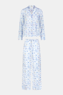 A woman smiles barefoot on a white background, hands in pockets, wearing Roller Rabbit's Starry Nights Lattice Long Sleeve Polo Pajamas—cozy loungewear crafted from soft Pima cotton.