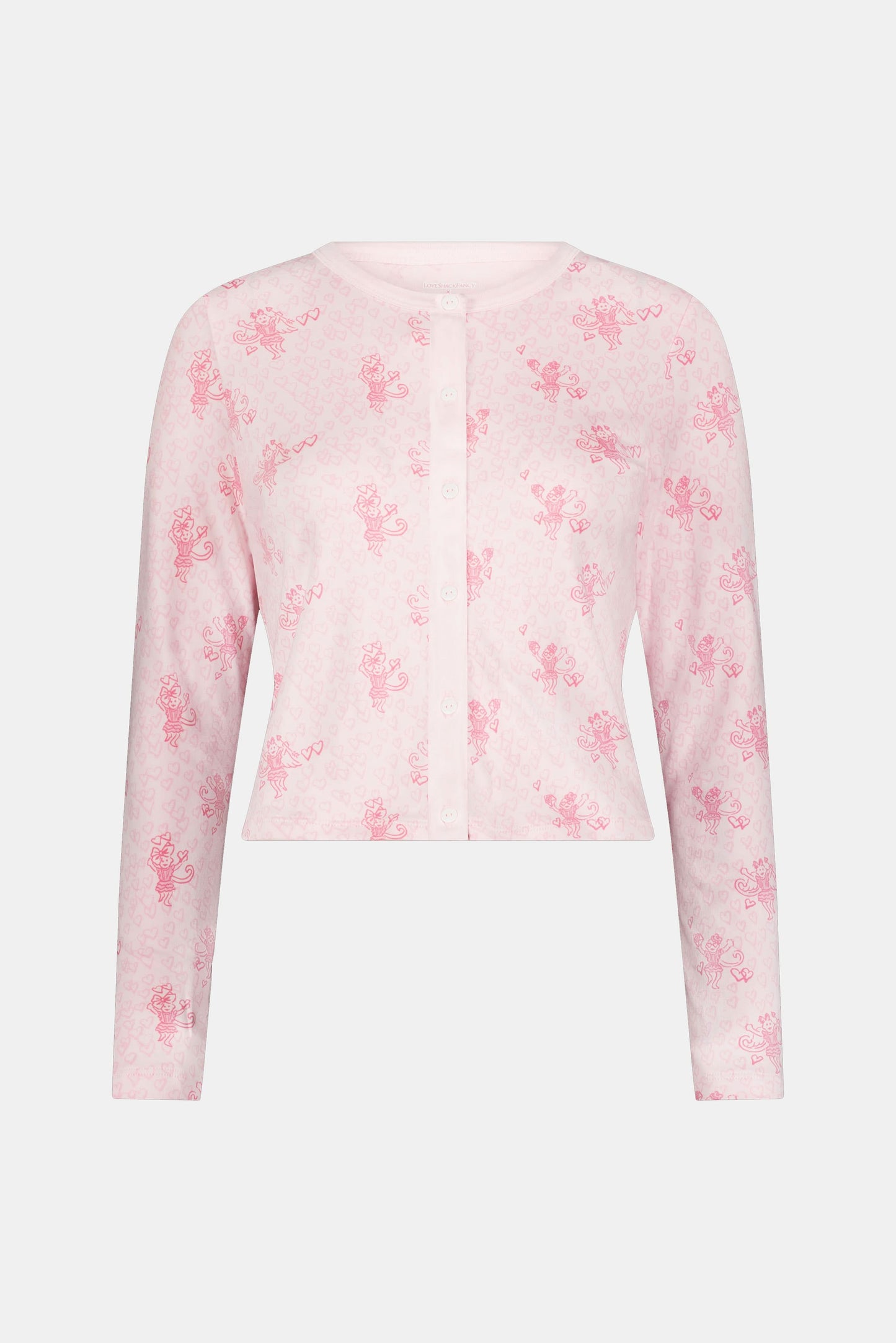 Wearing the Cupid's Kiss Nessa Cardigan by Roller Rabbit, a woman stands against a plain light background. The soft cardigan features a charming pink and white design with a delicate floral pattern, perfectly complemented by her matching sleep mask.