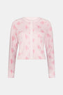 Wearing the Cupid's Kiss Nessa Cardigan by Roller Rabbit, a woman stands against a plain light background. The soft cardigan features a charming pink and white design with a delicate floral pattern, perfectly complemented by her matching sleep mask.