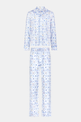 A man stands barefoot on a white background wearing Roller Rabbit's Mens Starry Nights Lattice Long Sleeve Polo Pajamas, featuring light blue and white patterns. He smiles with one hand in his pocket, highlighting the comfort of these matching PJs.