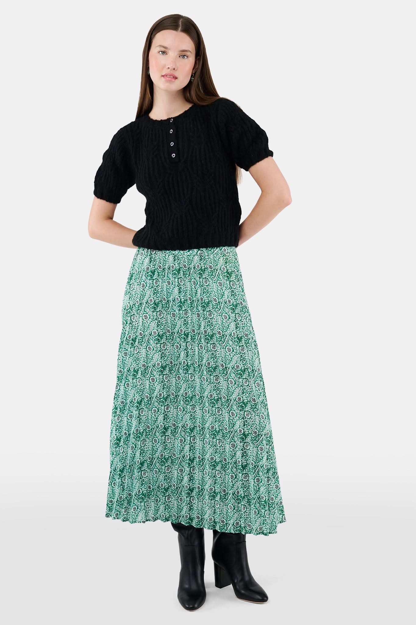 Someone wears the Roller Rabbit Fern Floral Megan Skirt—a green and white pleated maxi—paired with a black top, gold bracelets, and black heeled boots, shown from the waist down against a plain background.