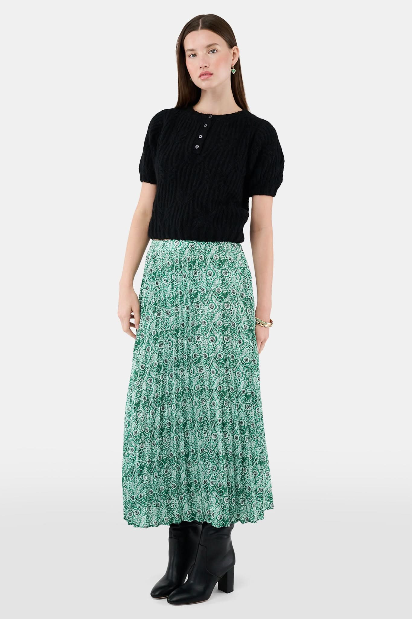 Someone wears the Roller Rabbit Fern Floral Megan Skirt—a green and white pleated maxi—paired with a black top, gold bracelets, and black heeled boots, shown from the waist down against a plain background.