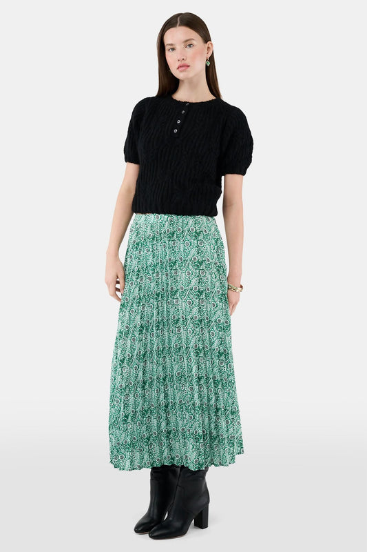 Someone wears the Roller Rabbit Fern Floral Megan Skirt—a green and white pleated maxi—paired with a black top, gold bracelets, and black heeled boots, shown from the waist down against a plain background.