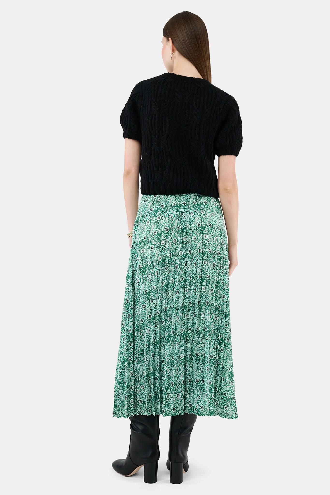 Someone wears the Roller Rabbit Fern Floral Megan Skirt—a green and white pleated maxi—paired with a black top, gold bracelets, and black heeled boots, shown from the waist down against a plain background.