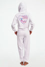 A person stands barefoot in Roller Rabbit O.C. Monkey Sweatpants and a matching hoodie, featuring colorful embroidered and printed graphics near the left pocket. The background is plain white.