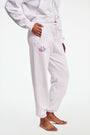 A person stands barefoot in Roller Rabbit O.C. Monkey Sweatpants and a matching hoodie, featuring colorful embroidered and printed graphics near the left pocket. The background is plain white.