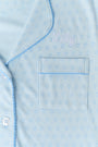 A woman wears Roller Rabbit's Hearts Tonal Wyatt Polo Pajamas—light blue, short-sleeved Pima cotton with a collar and chest pocket—paired with matching ruffled shorts, standing against a plain light background.
