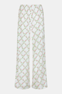 Someone stands against a plain white background wearing Roller Rabbit's Raspberry Garden Monroe Pant—loose white loungewear pants with a pink and green floral print—paired with maroon slippers adorned with white floral details.