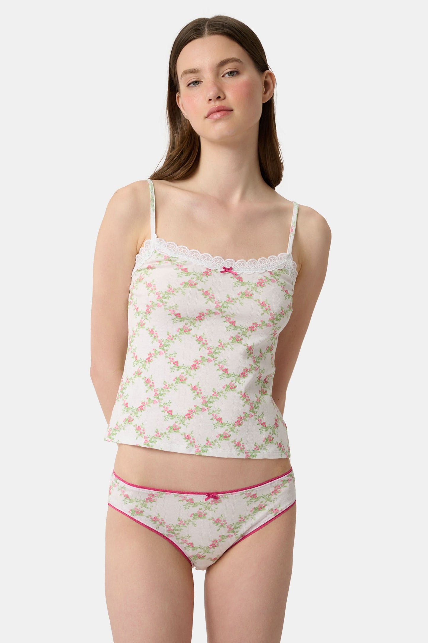 A person wearing the Roller Rabbit Raspberry Garden Gwen Bikini, a matching white camisole and vintage-inspired underwear set with a pink floral pattern and pink trim, shown from mid-torso to upper thighs.