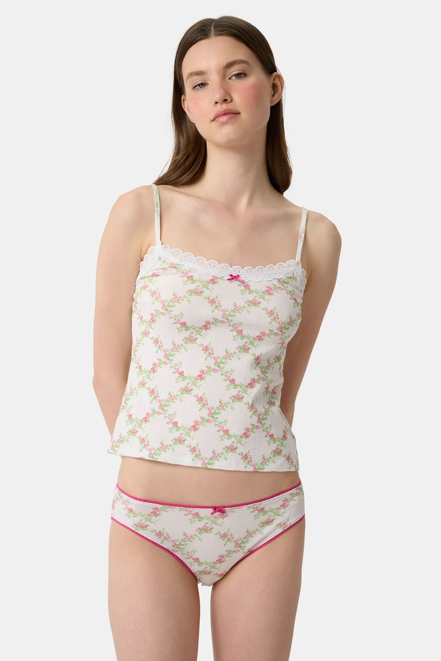 A person wearing the Roller Rabbit Raspberry Garden Gwen Bikini, a matching white camisole and vintage-inspired underwear set with a pink floral pattern and pink trim, shown from mid-torso to upper thighs.