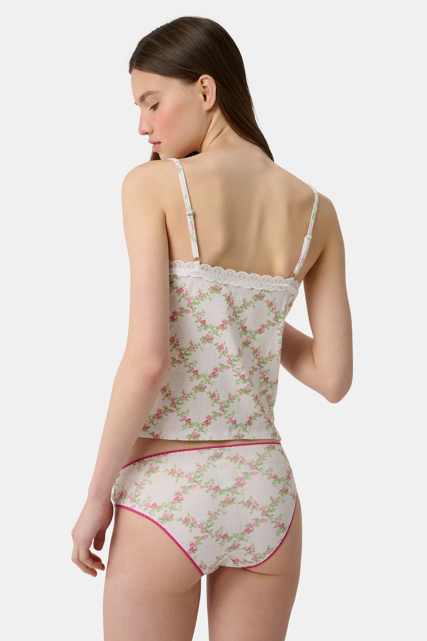 A person wearing the Roller Rabbit Raspberry Garden Gwen Bikini, a matching white camisole and vintage-inspired underwear set with a pink floral pattern and pink trim, shown from mid-torso to upper thighs.