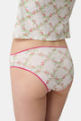 A person wearing the Roller Rabbit Raspberry Garden Gwen Bikini, a matching white camisole and vintage-inspired underwear set with a pink floral pattern and pink trim, shown from mid-torso to upper thighs.