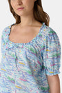 A woman wears the Roller Rabbit Regatta Preston Set, a cotton voile two-piece with a pastel coastal print, featuring a short-sleeve top with gathered neckline and matching shorts, standing against a plain white background.