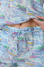 A woman wears the Roller Rabbit Regatta Preston Set, a cotton voile two-piece with a pastel coastal print, featuring a short-sleeve top with gathered neckline and matching shorts, standing against a plain white background.