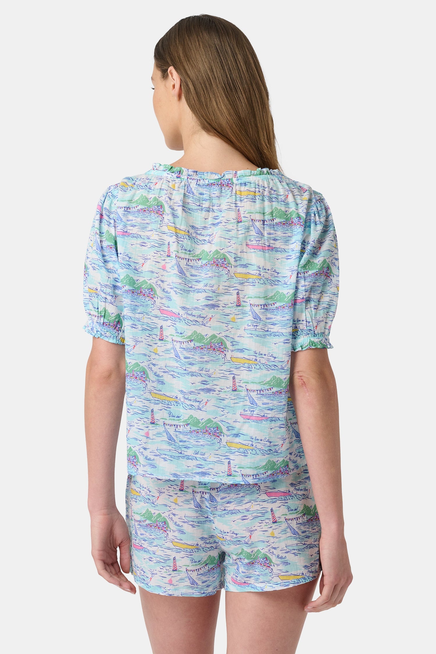 A woman wears the Roller Rabbit Regatta Preston Set, a cotton voile two-piece with a pastel coastal print, featuring a short-sleeve top with gathered neckline and matching shorts, standing against a plain white background.