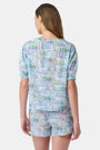 A woman wears the Roller Rabbit Regatta Preston Set, a cotton voile two-piece with a pastel coastal print, featuring a short-sleeve top with gathered neckline and matching shorts, standing against a plain white background.