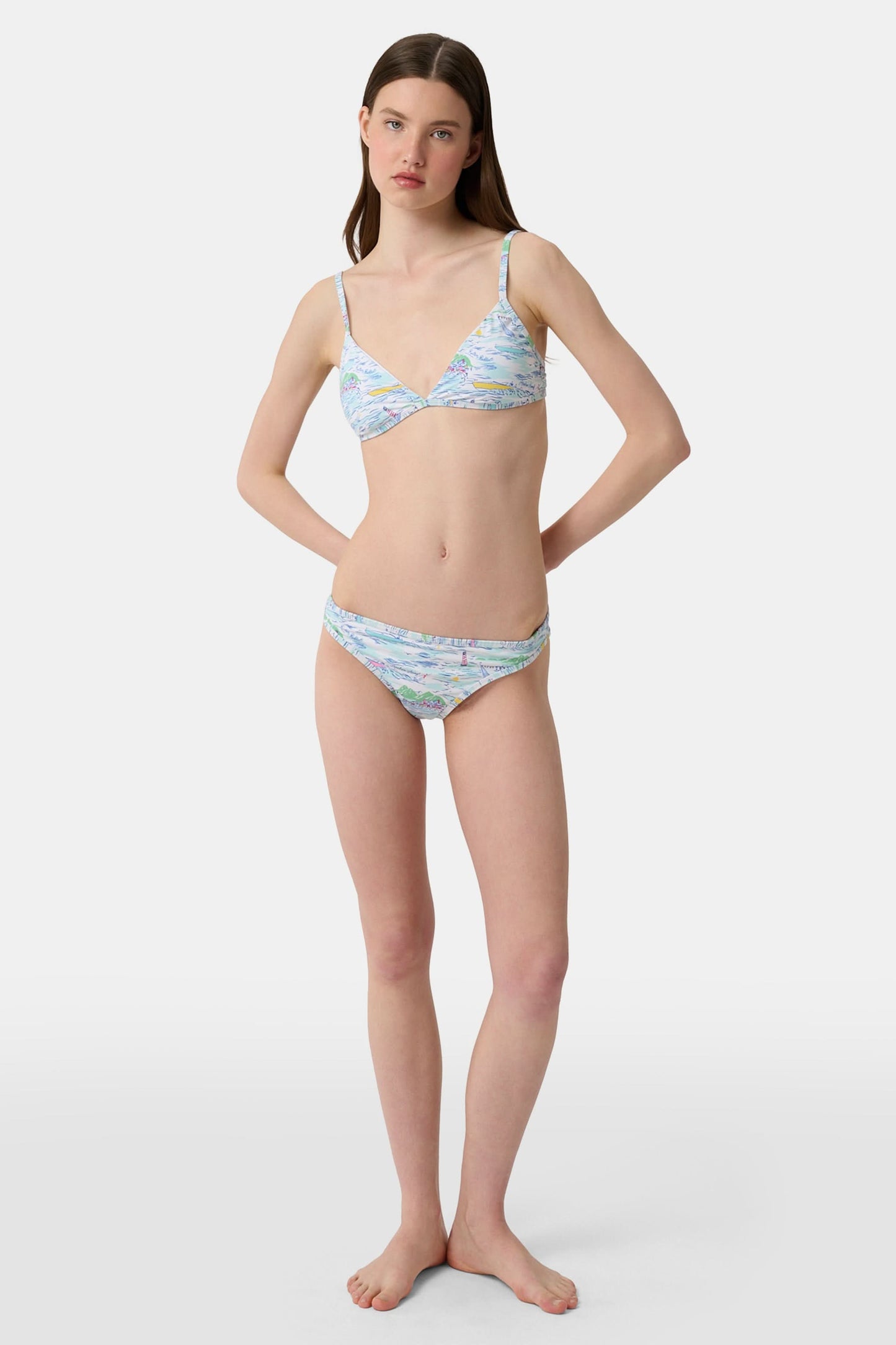 A person wears the Roller Rabbit Regatta Marais Bikini Bottom, featuring a colorful nautical print with boats and lighthouses. The UPF 50+ swimwear offers sun protection. Image is cropped from chest to upper thighs.