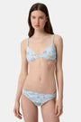 A woman with long brown hair smiles softly, wearing the Regatta Marais Bikini Top by Roller Rabbit in a nautical print, standing against a plain white background.