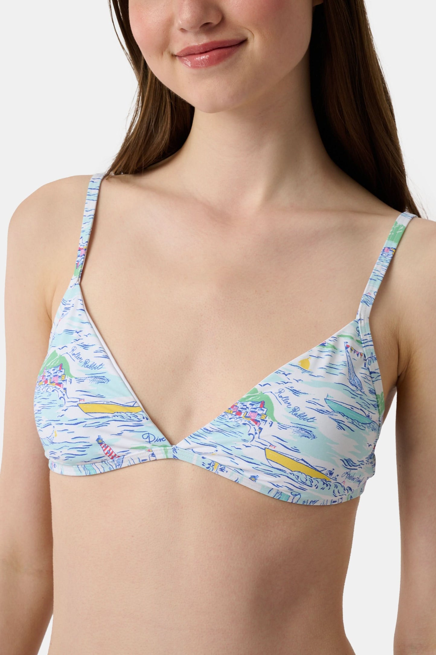 A woman with long brown hair smiles softly, wearing the Regatta Marais Bikini Top by Roller Rabbit in a nautical print, standing against a plain white background.