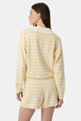 A person wears Roller Rabbit’s Striped Brie Short—a knit yellow and white horizontal striped short with a white drawstring at the elastic waistband and hands tucked in the front pockets.