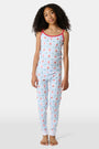 A young girl stands barefoot, smiling against a light background. She wears the Roller Rabbit Kids 4th of Jemina Noa Set—matching white Pima Cotton pajamas with red trim and a colorful flowers, butterflies, and birds print.