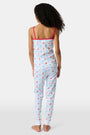 A young girl stands barefoot, smiling against a light background. She wears the Roller Rabbit Kids 4th of Jemina Noa Set—matching white Pima Cotton pajamas with red trim and a colorful flowers, butterflies, and birds print.