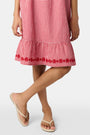 A young girl in the Roller Rabbit Kids Gingham Teagan Dress with an embroidered hem stands barefoot on a boat deck by the water, sunlight shimmering on the surface.