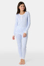 A young girl with long brown hair stands barefoot in Roller Rabbit Kids Seaside Knots Juniper Pajamas, featuring matching white and light blue knot print on soft Pima fabric with long sleeves and button details, against a plain light background.