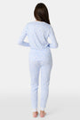 A young girl with long brown hair stands barefoot in Roller Rabbit Kids Seaside Knots Juniper Pajamas, featuring matching white and light blue knot print on soft Pima fabric with long sleeves and button details, against a plain light background.