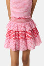 A child wears the Roller Rabbit Kids Starry Dot Sami Skirt in pink and red with star and polka dot patterns, paired with a pink smocked top, standing against a plain light background.