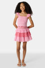 A child wears the Roller Rabbit Kids Starry Dot Sami Skirt in pink and red with star and polka dot patterns, paired with a pink smocked top, standing against a plain light background.
