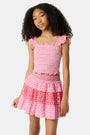 A young girl wears the Roller Rabbit Kids Starry Dot Tory Top in pastel pink with flutter sleeves, paired with a matching skirt featuring red stars and white polka dots. Only her torso and part of her face are visible.