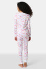 A young girl smiles barefoot in Roller Rabbit Kids Summer Memories Pajamas, made from soft Pima Cotton with playful, colorful prints on white. She stands against a light gray background. Made in Peru.