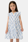 A young girl with long brown hair wears the Roller Rabbit Kids Rosa Ditsy Floral Pami Dress, made from cotton voile with blue-green block print and ruffled sleeves, standing against a plain light background, looking slightly to the side.