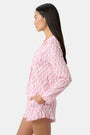 Wearing the Roller Rabbit Rosa Ditsy Monkey Hayden Pajamas—a pink and white set with a small anchor print, long-sleeve button-up top, and ruffled shorts—a person stands against a plain light background, smiling slightly.