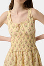 A young woman models the Roller Rabbit Rosa Ditsy Floral Penny Dress, a light yellow sundress with a floral pattern, gathered bodice, and gently flared skirt, set against a plain white background.