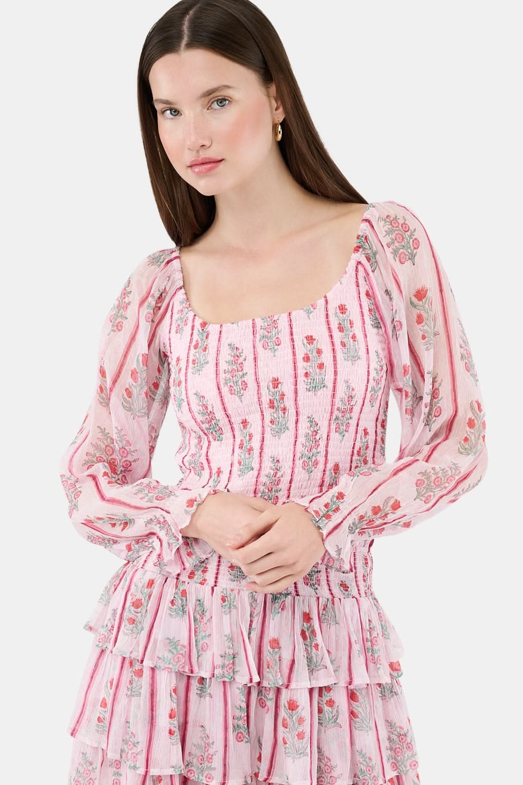 A woman with long brown hair models the Roller Rabbit Rose Ribbon Morgana Top—a pink, floral long-sleeve blouse—against a plain light background.