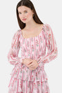 A woman with long brown hair models the Roller Rabbit Rose Ribbon Morgana Top—a pink, floral long-sleeve blouse—against a plain light background.
